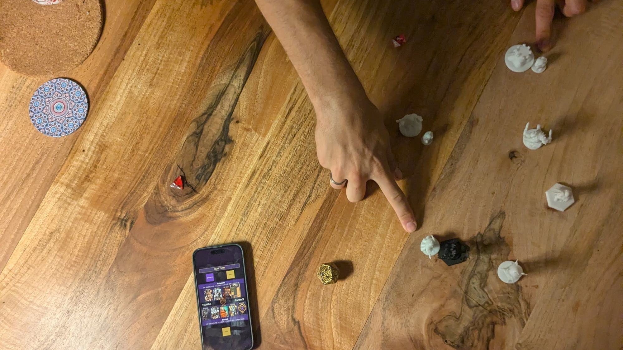 Hand zeigt auf eine Warconicas-Miniatur neben Würfeln und Smartphone mit der App