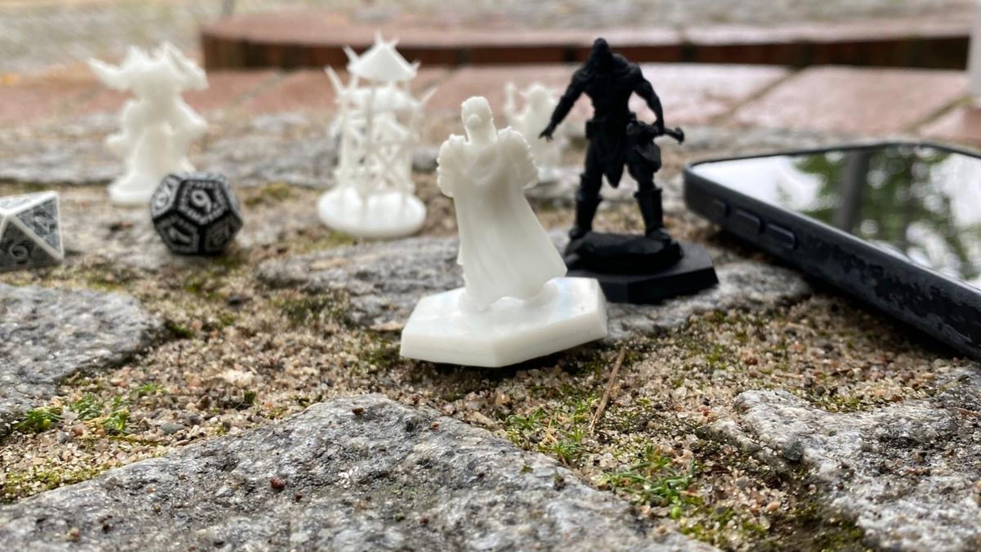 Warconicas-Miniaturen, Würfel und Smartphone mit geöffneter App auf Stein